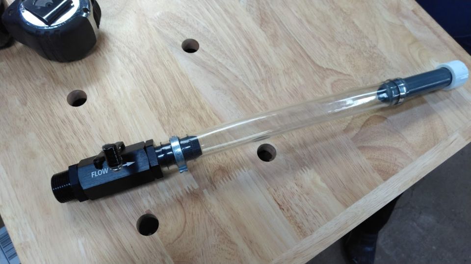 Clear tube with flow valve and white cap on a wooden surface.