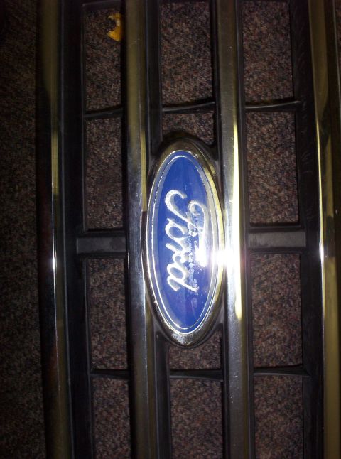 1988 Ford Bronco - The blue Ford emblem is centered on a chrome grille with vertical bars.
