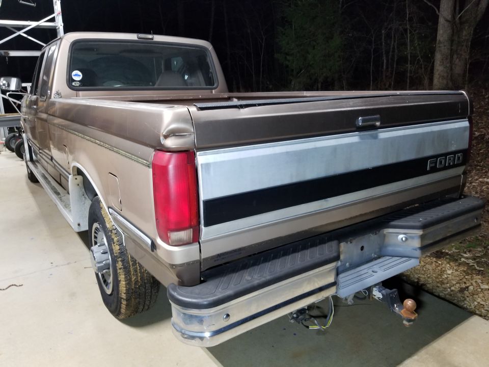 Night photo of a brown Ford pickup from rear driver side showing tailgate, chrome bumper, and trailer hitch