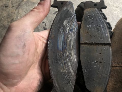 1994 Ford Bronco - Worn brake pads are held up for inspection, revealing significant damage and scoring on one of the pads.