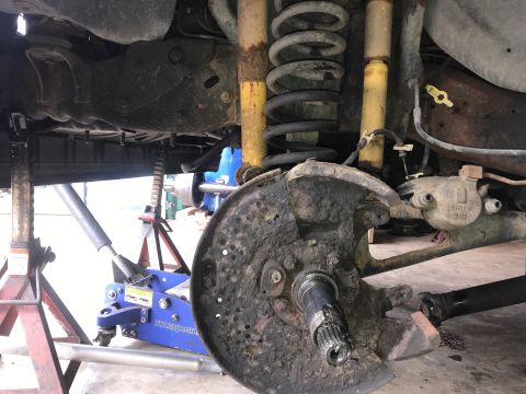1994 Ford Bronco - The vehicle's front suspension and brake system are disassembled and supported by various automotive repair tools.