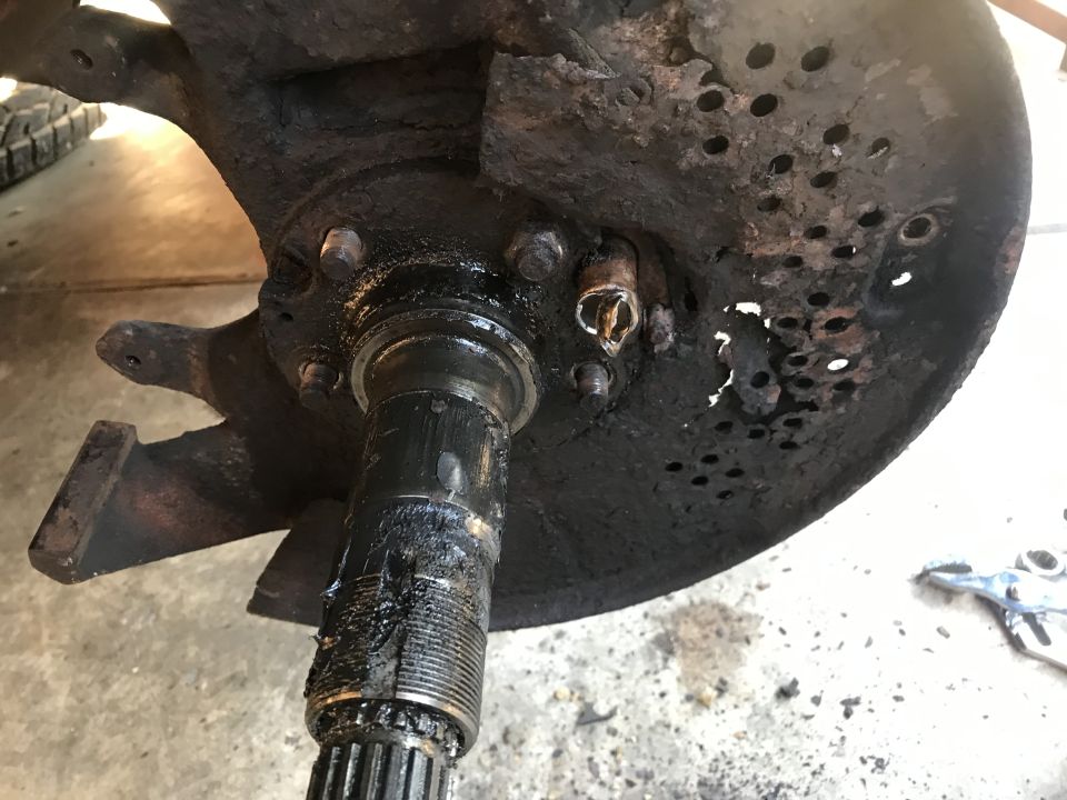 Wheel hub assembly with damaged rotor and caliper bracket. Greasy splined shaft visible
