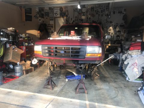 1994 Ford Bronco - Front end of a 1994 Ford Bronco disassembled in a garage, with parts laid out on the hood.