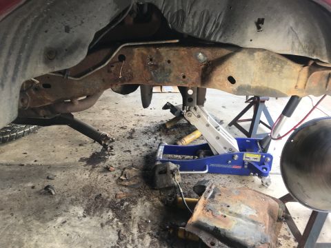 1994 Ford Bronco - The underside of a vehicle is shown with significant rust on the frame and suspension components, supported by jacks.