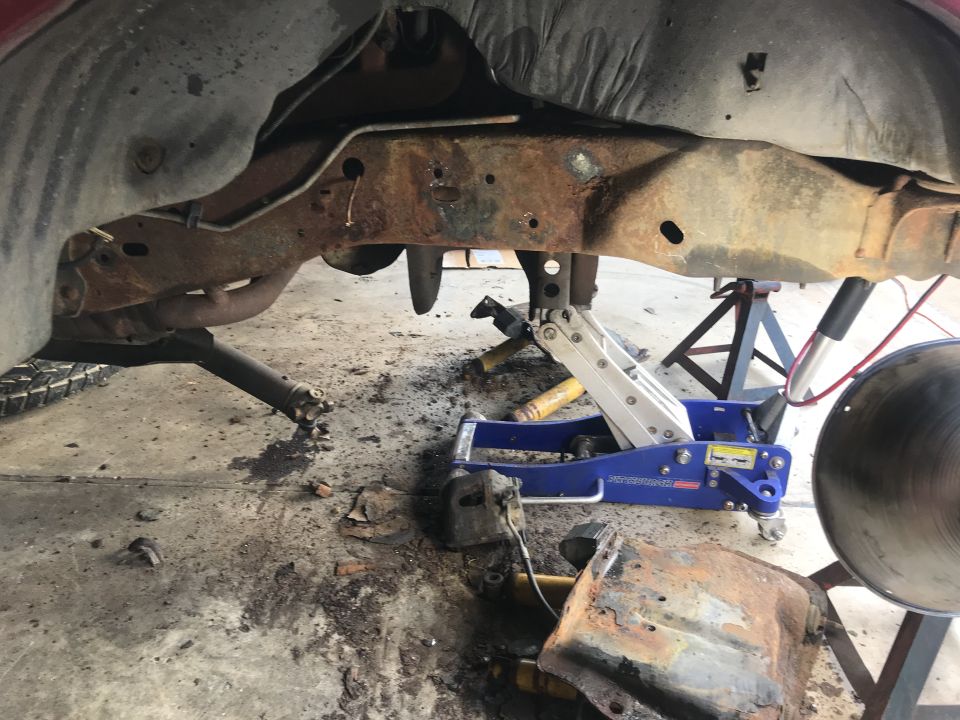 rusted frame, suspension, and jack stands under a vehicle