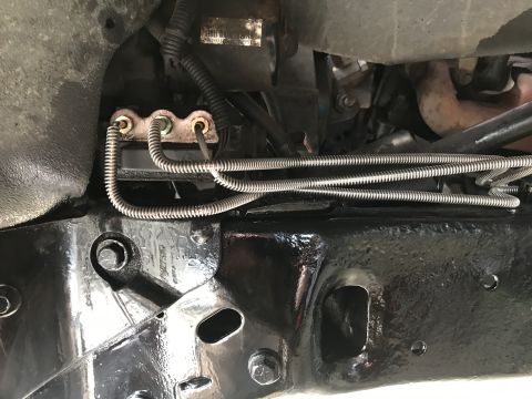 1994 Ford Bronco - Close-up view of the vehicle's brake lines and chassis components, showing metal tubing and protective shielding.