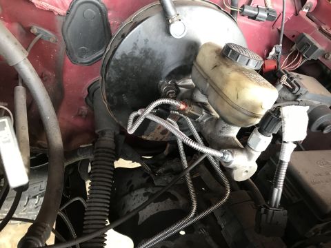 1994 Ford Bronco - Close-up of a vehicle's brake booster and master cylinder assembly, showing brake lines and electrical connectors.