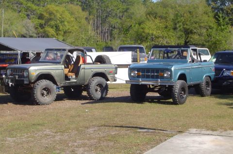 1974 Ford Bronco - Two Ford Broncos, one green and one blue, are parked outdoors on a grassy area.