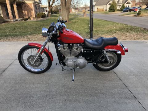 2002 Harley-Davidson Sportster Custom - A red 2002 Harley-Davidson Sportster Custom motorcycle is shown from the side, parked on a concrete driveway in front of a house.