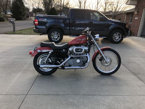 2002 Harley-Davidson Sportster Custom - A red Harley-Davidson motorcycle is parked in front of a dark blue pickup truck in a driveway.