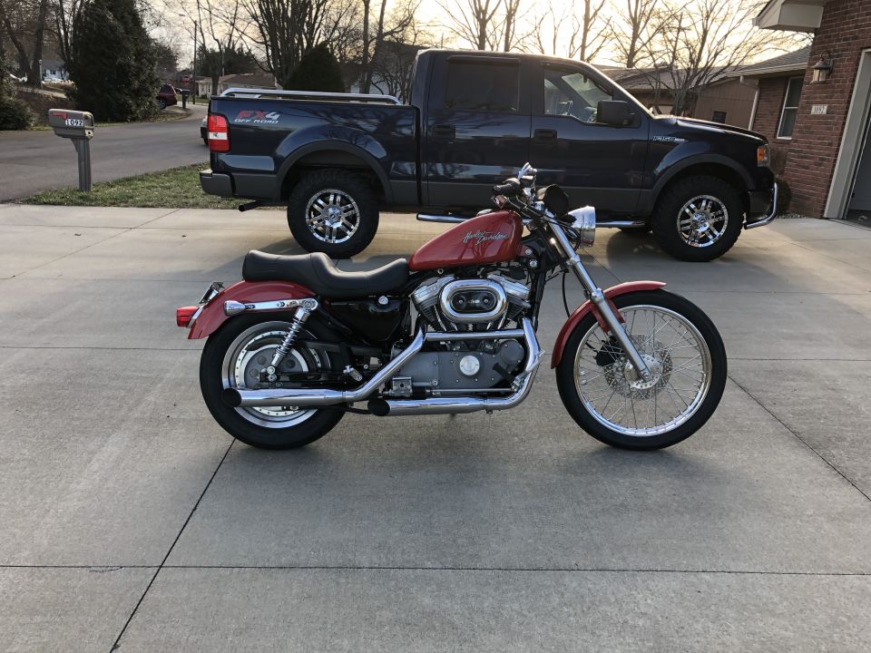 Red Harley-Davidson Sportster motorcycle parked in front of a dark blue pickup truck