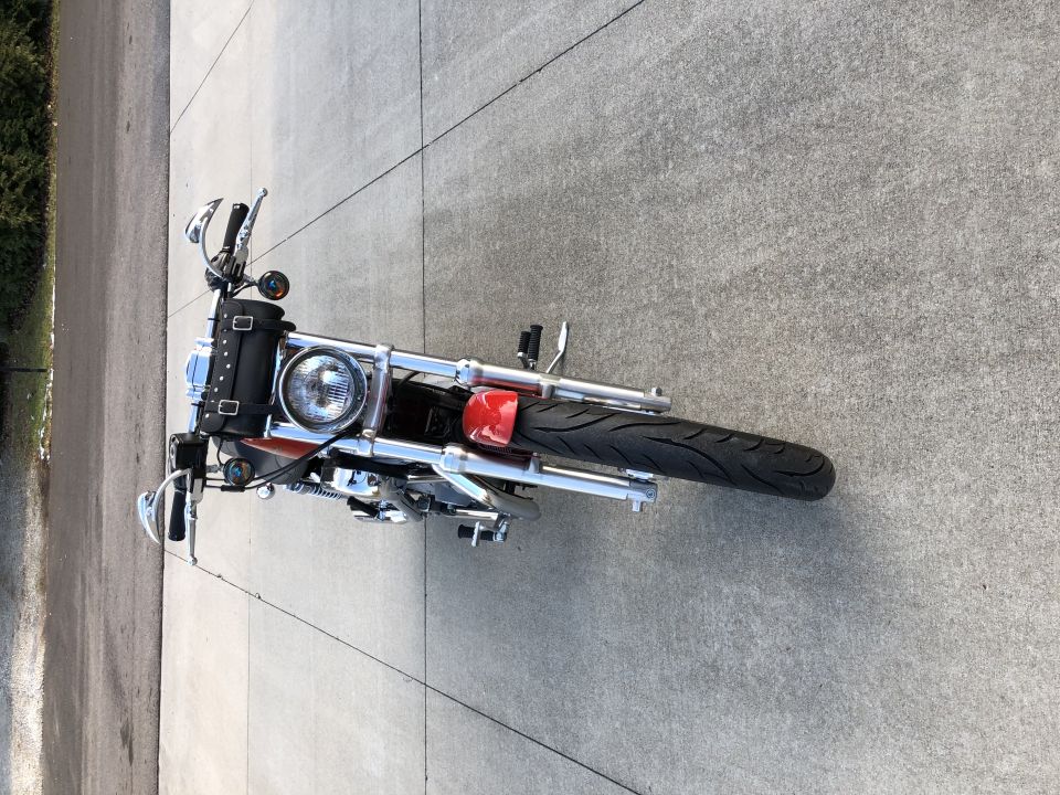 Motorcycle with chrome handlebars, a black leather tool bag, and a red tail light, viewed from above