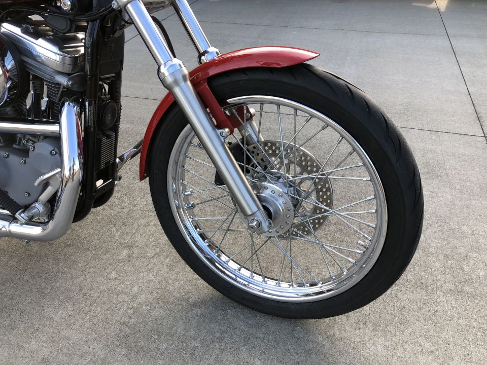 Red motorcycle front wheel, fender, and chrome engine details. 2002 Harley-Davidson Sportster Custom