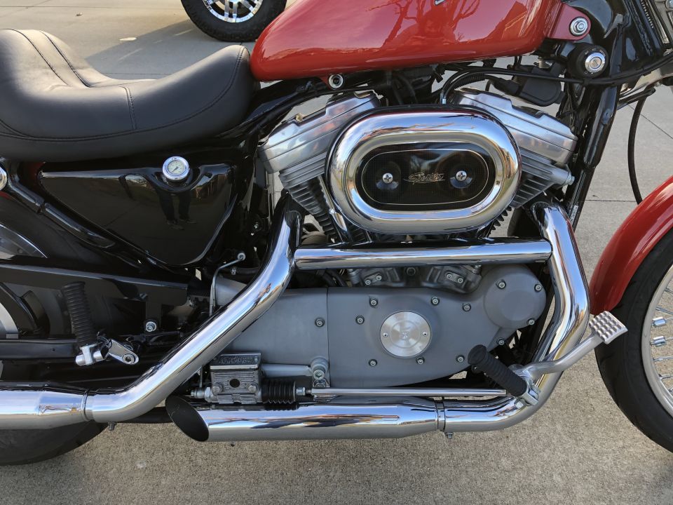 Close-up of a Harley-Davidson Sportster engine and exhaust pipes. Chrome air cleaner cover has text on it