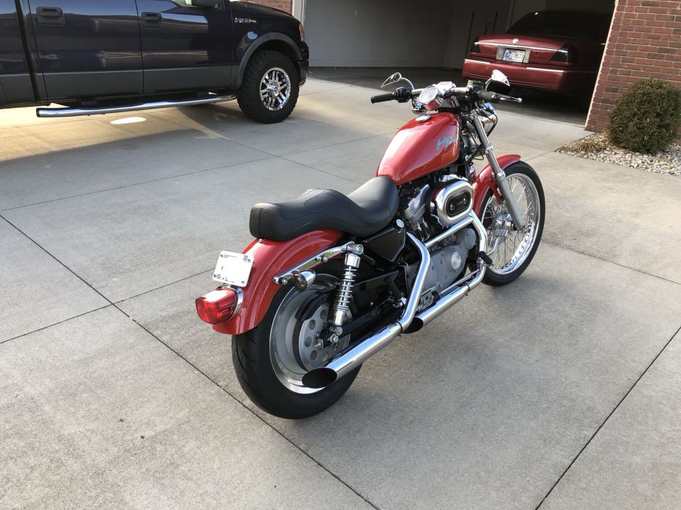 Red motorcycle parked on a driveway next to a dark blue pickup truck and a red car in a garage
