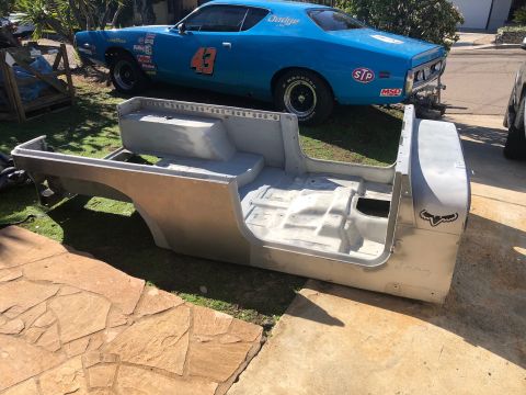 1992 Jeep Wrangler - A bare Jeep CJ-7 body tub sits on grass, with a blue Dodge Charger in the background.