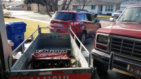 1985 Ford Bronco - Engine block being transported in a trailer, with other vehicles visible in the background.