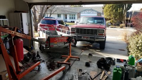 1985 Ford Bronco - A red pickup truck is parked in a garage next to a U-Haul trailer, with an SUV visible behind it.
