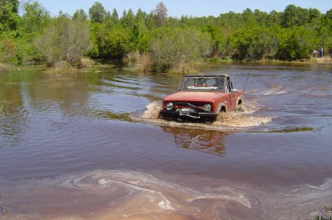 1974 Ford Bronco - A red 1974 Ford Bronco navigates through a shallow body of water, its winch visible on the front bumper.