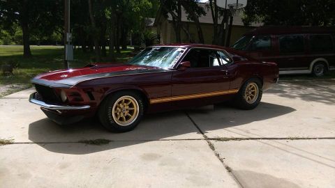 1970 Ford Mustang - A classic maroon 1969 Ford Mustang is parked on a concrete driveway, with a van visible behind it.