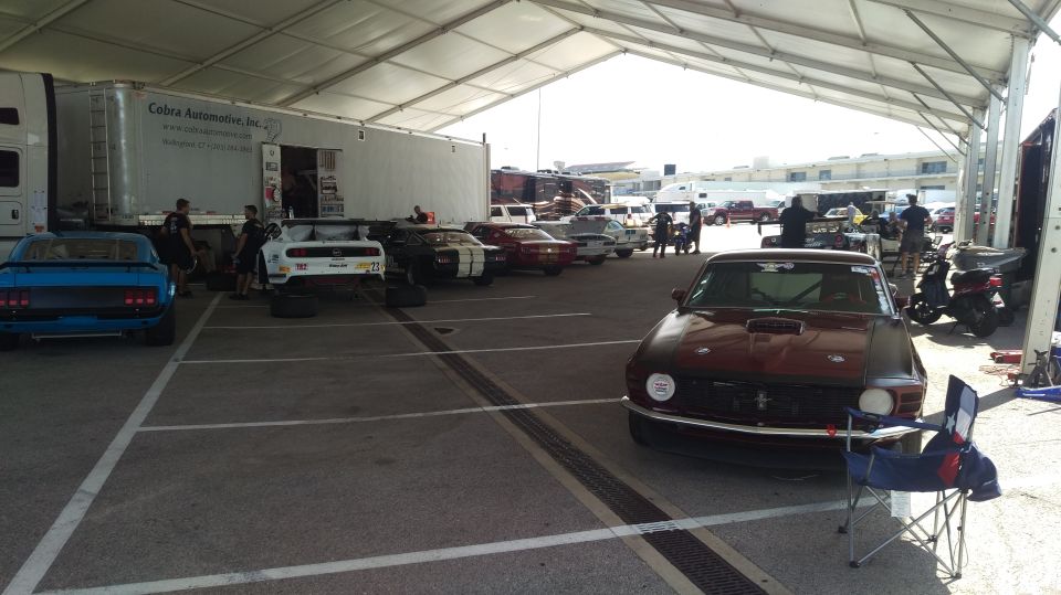 Maroon Mustang fastback parked in a vintage racing paddock tent with other race cars