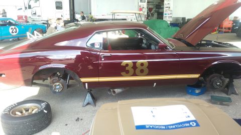 1970 Ford Mustang - A maroon 1970 Ford Mustang coupe is shown on jack stands with its hood open, undergoing maintenance.
