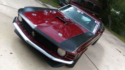 1970 Ford Mustang - Front 3/4 view of a dark red 1970 Ford Mustang, a prominent hood scoop and black racing stripes.