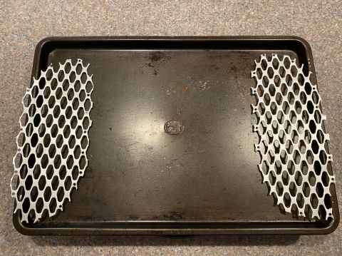 2000 Pontiac Grand Prix - Two silver honeycomb grilles are placed on a dark baking sheet.