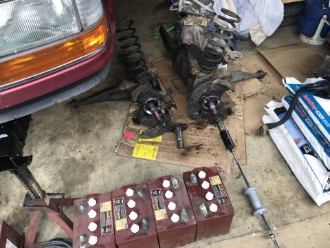 1994 Ford Bronco - Front suspension parts and batteries laid out for work in a garage.