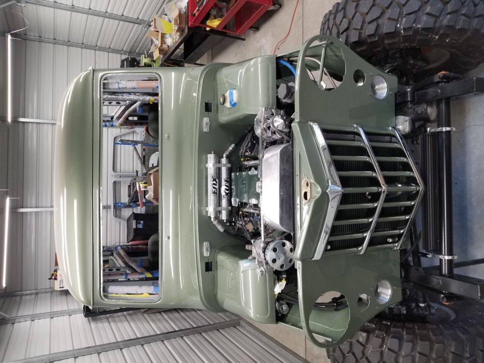 olive green truck body with engine exposed, large tires, in a garage