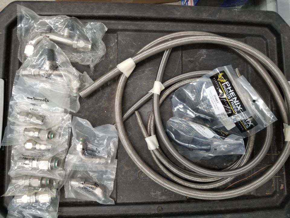 Braided stainless steel brake lines and assorted fittings in plastic packaging on a black tray