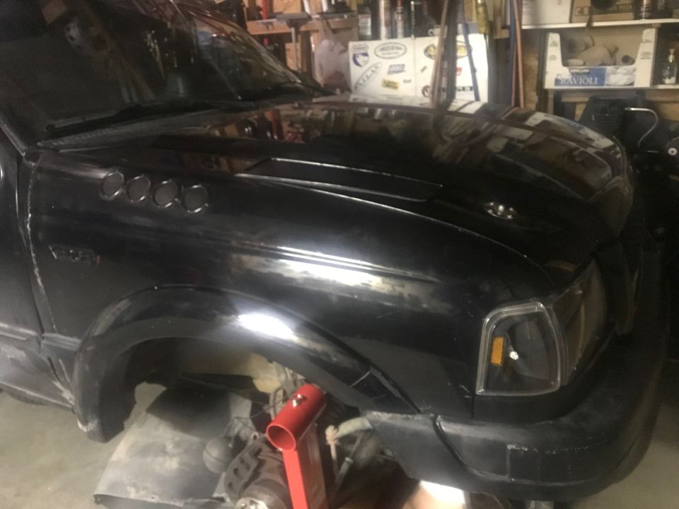 Black SUV with circular vents on fender, jacked up for repair