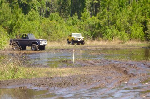 1974 Ford Bronco - Two Ford Broncos, one first-generation and one second-generation, navigate a wet, muddy landscape.