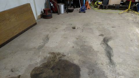 1979 Chevrolet Camaro - The image shows a garage floor with several dark oil stains, a large wooden panel leaning against the wall, and various tools in the backgr…