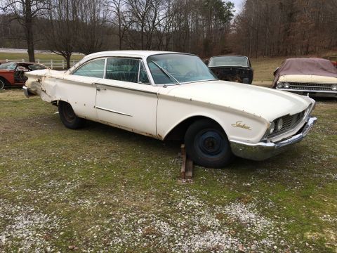 1960 Ford Starliner - White 1960 Ford Starliner coupe sits in a grassy lot with other vehicles nearby.