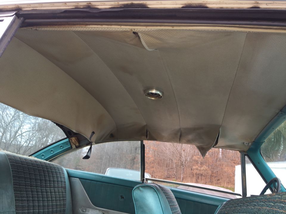 Car interior showing torn headliner, teal seats, and a steering wheel