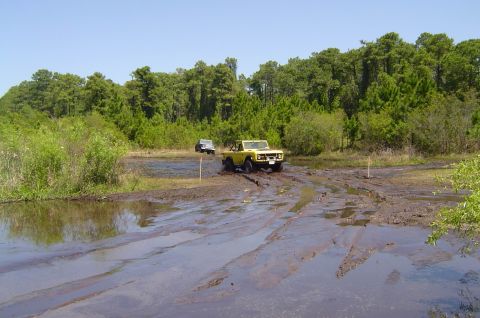 1974 Ford Bronco - A yellow 1974 Ford Bronco tackles a muddy obstacle course with another vehicle in the background.