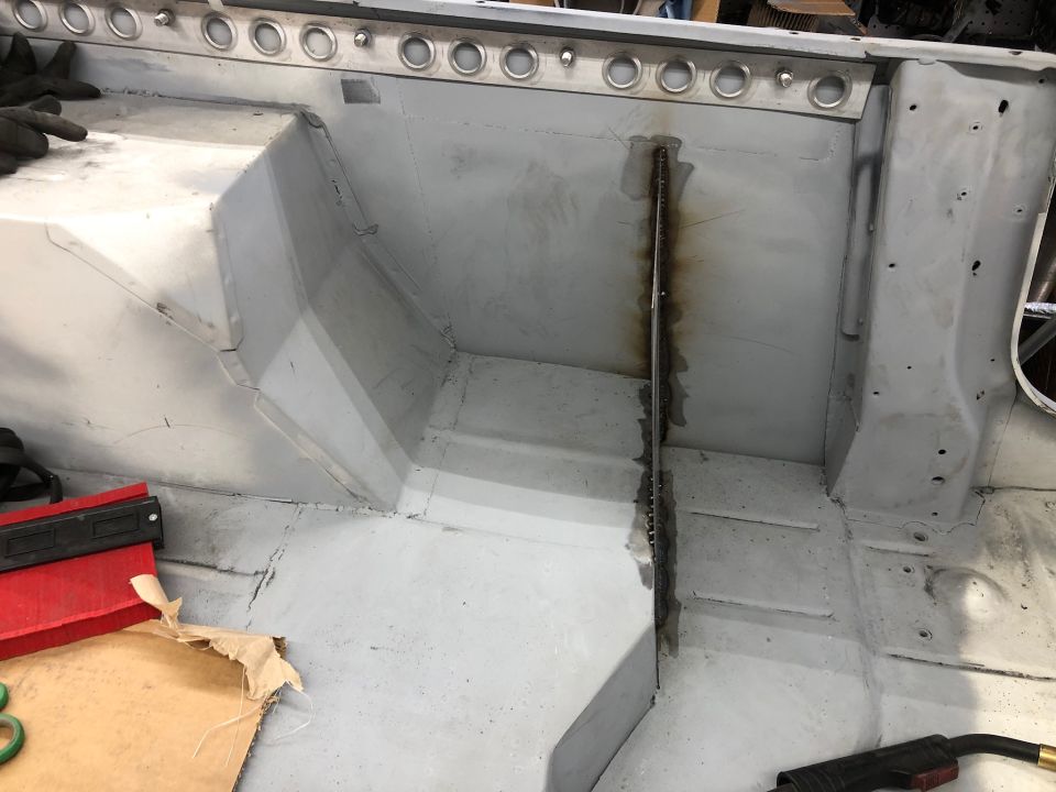 Interior of a vehicle body with gray primer, showing metal seams and bracing