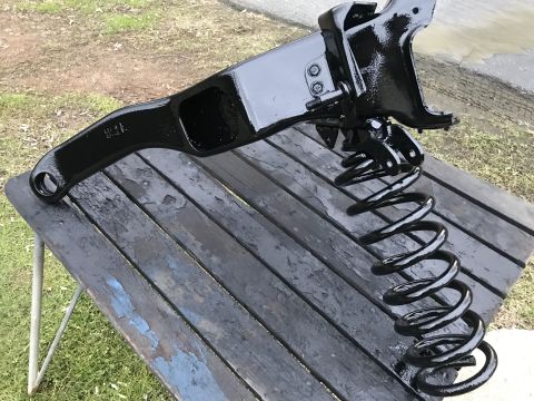 1994 Ford Bronco - Painted suspension component with coil spring sits on weathered wooden planks outdoors.