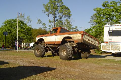 1974 Ford Bronco - This heavily modified Ford pickup truck is parked outdoors next to a recreational vehicle.