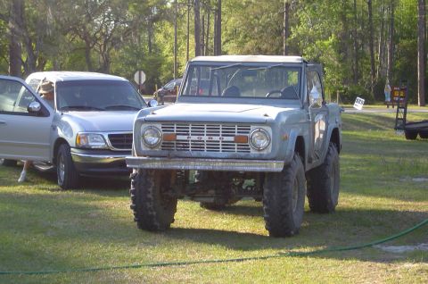 1974 Ford Bronco - A light blue 1974 Ford Bronco with large off-road tires is parked on a grassy field next to a silver pickup truck.