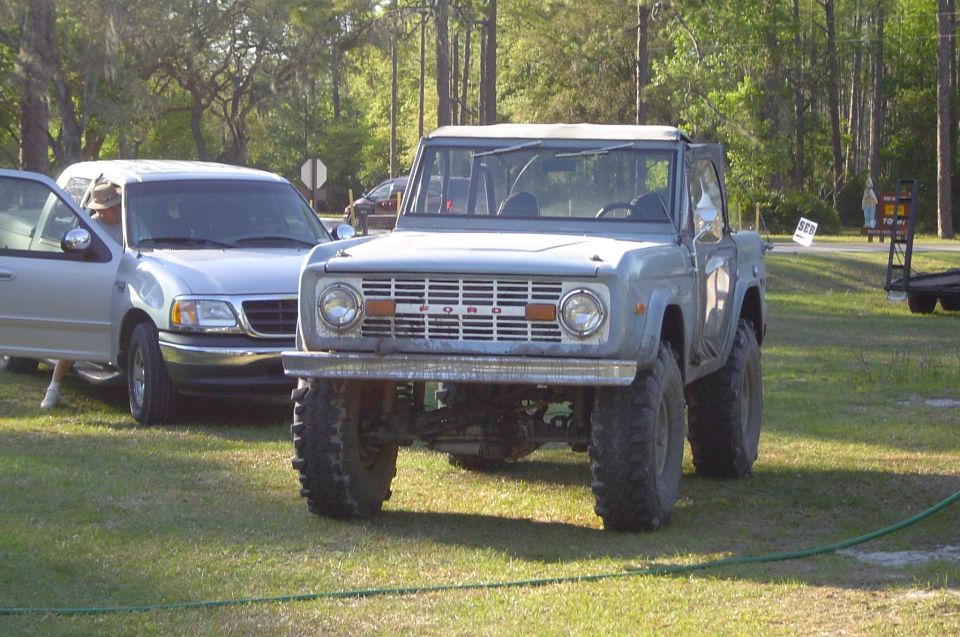 Light blue early Ford Bronco with tan soft top and mud tires parked on grass
