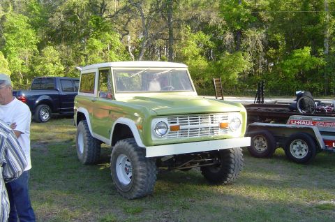 1974 Ford Bronco - A 1974 Ford Bronco is parked on grass next to a U-Haul trailer and a blue pickup truck.