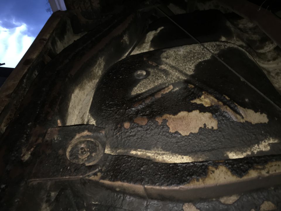 Underside of a car with heavy undercoating and some rust showing