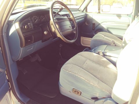 1996 Ford Bronco - The interior of a light blue vehicle shows cloth seats, a steering wheel, and dashboard instrumentation.