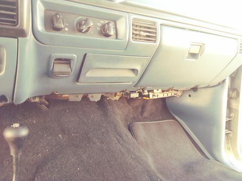 1996 Ford Bronco - The interior of a vehicle shows the dashboard controls, floor carpet, and a manual gear shifter.