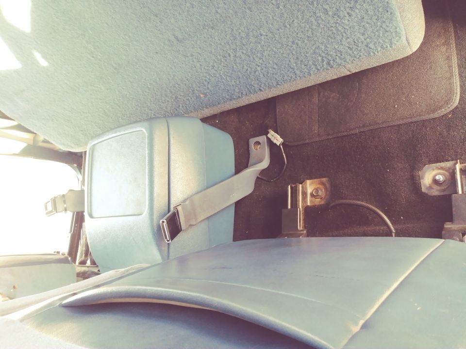 Vehicle interior showing a light blue seatbelt buckle and strap attached to a bracket, with part of a seat and dashboard visible