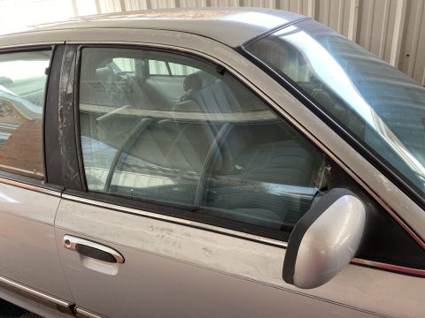 1994 Ford Crown Victoria - The side profile of a silver sedan reveals its interior with fabric seats and exterior details like the side mirror.