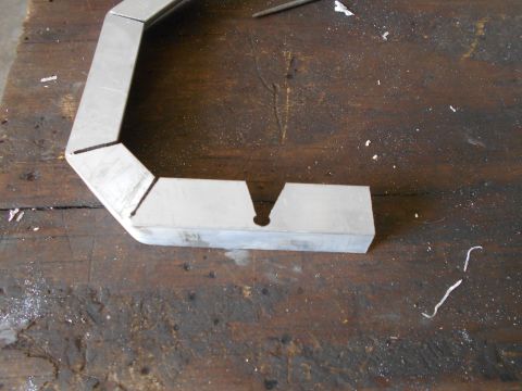 1992 Ford Bronco - Metal bracket with angled cuts and a central hole on a wooden workbench.