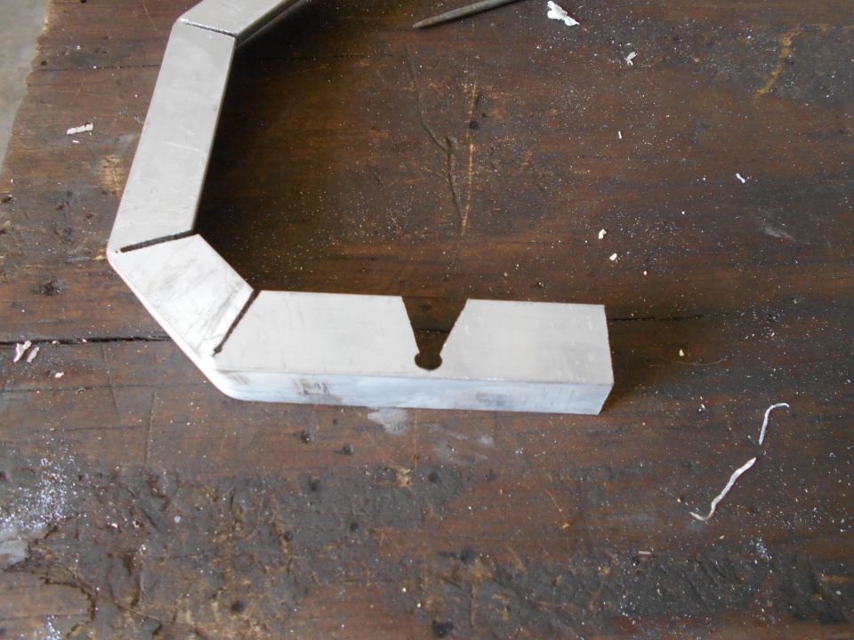 Metal bracket with angled cuts and a central hole, resting on a wooden workbench